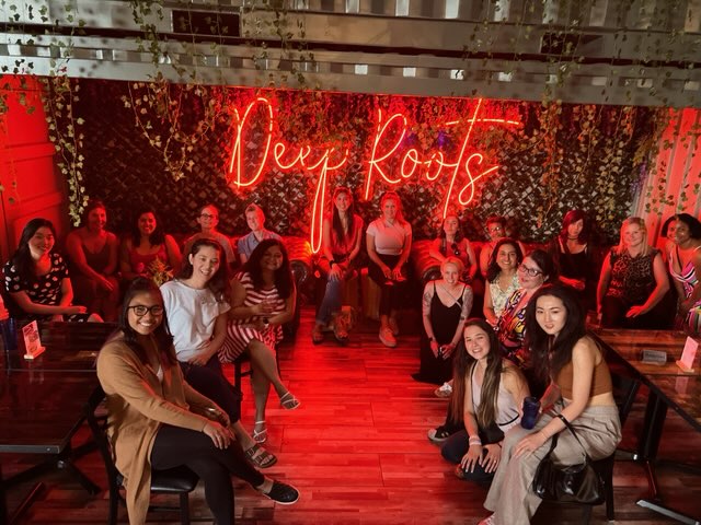Women&TECH members at a social event with neon Deep Roots sign